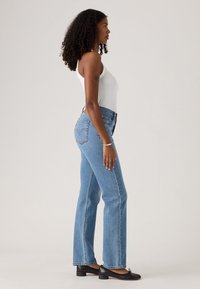 Jean droits taille haute bleu clair, en denim, avec un design classique à cinq poches. Associé à un débardeur blanc et des ballerines noires.