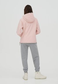 Lyserød hættejakke med lynlås foran, parret med grå sweatpants. Sættet har ribbede manchetter og beige høje sneakers.