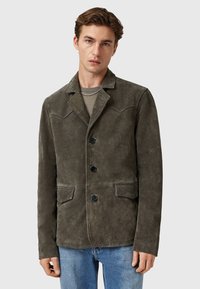 Giacca in suede di un verde oliva scuro, con colletto a punta, tre bottoni, due tasche frontali e dettagli a yoke in stile western.