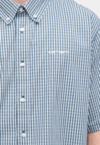 Πουκάμισο με κοντά μανίκια και κουμπιά σε μπλε και λευκά καρό, με μυτερό γιακά, μονόχρωμα κουμπιά και κεντημένο λογότυπο στο στήθος.