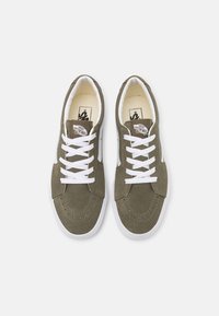 Olivově zelené semišové tenisky s bílými tkaničkami a gumovými podrážkami. Mají klasické logo Vans na jazyku a design bočního pruhu.