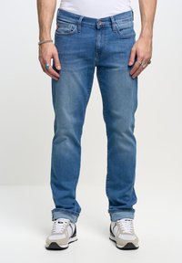 Vaqueros de mezclilla azul claro con un corte recto, que presentan un diseño clásico de cinco bolsillos y costuras visibles. Combinados con zapatillas grises y blancas.
