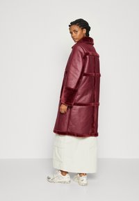 Bordeaux faux læderjakke med en struktureret overflade, der har en bred krave, bløde elementer og et løst, mellemlangt design.