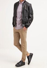 Zwarte leren bomberjack, licht geruit shirt, khaki chino's en zwarte sneakers. Het jasje heeft een ritszak, een relaxte pasvorm en geribde manchetten.