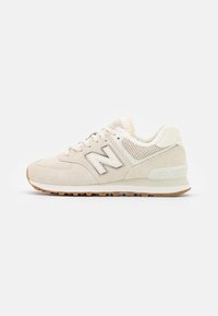 Béžové tenisky New Balance se svrškem z semiše a síťoviny, bílou mezipodešví, gumovou podrážkou a polstrovaným límcem s fleecovou podšívkou, boční pohled.