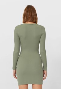 Robe côtelée à manches longues de couleur vert olive. Silhouette ajustée avec un col arrondi et un ourlet à mi-cuisse. Texture lisse.