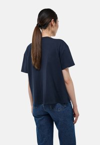 T-shirt en coton bleu marine à manches courtes, coupe décontractée et col rond. Il a un ourlet visible et est assorti à un jean bleu.