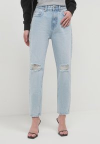 Jeans taille haute bleu clair en denim, dotés de déchirures aux genoux, d'une coupe droite et de bords légèrement effilochés.