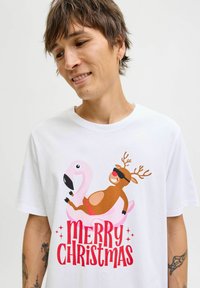 Witte katoenen t-shirt met een afbeelding van een rendier op een roze flamengo, met "MERRY CHRISTMAS" in rode en roze letters eronder.