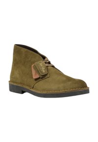 Stivale alla caviglia in suede verde oliva con punta rotonda, chiusura con lacci e dettagli cuciti. Presenta un piccolo etichetta del marchio sul lato.