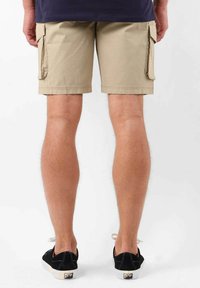 Shorts cargo beiges avec deux poches latérales, fabriqués à partir d'un matériau léger, à ourlet au genou, associés à des baskets noires.