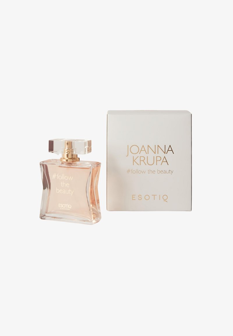 Przezroczysta szklana butelka o szlifowanej formie, z jasnoróżowym płynem i kwadratową nakrętką. Towarzyszy jej biała pudełko z złotym napisem.