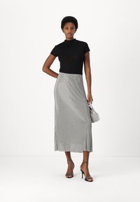 Black fitted shirt, silver shimmering long skirt, strappy black heels, and small white handbag. Smooth fabric with subtle texture and shine.