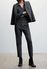 Donkergrijs op maat gemaakt pak met een getailleerd jasje, een lange mouw top en slanke broek, aangevuld met zwarte hoge hakken enkelboots.