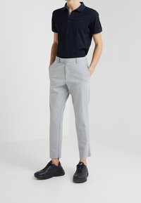 Marinblå polotröja med flerfärgad kragdetalj, grå tapered byxor och svarta sneakers. Tyget verkar slätt, med en avslappnad men åtsittande design.