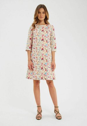 Robe mi-longue à motifs floraux en crème, dotée de manches trois-quarts et d'une silhouette droite. Associée à des sandales olive à lanières.