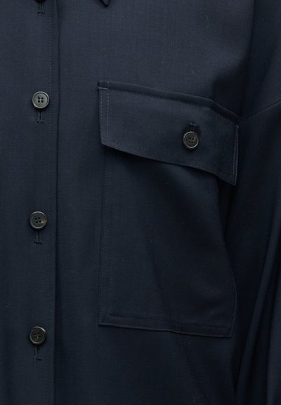 Σκούρο μπλε πουκάμισο με μαύρα κουμπιά και μία μπροστινή τσέπη στο στήθος με καπάκι και κουμπί, κατασκευασμένο από απαλό ύφασμα.