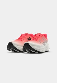 Une paire de chaussures de course corail rose et blanches avec des semelles noires et des logos New Balance sur les côtés, présentée de face sur un fond blanc.