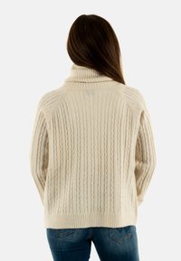 Maglione a rete di colore crema con colletto alto, orlo e polsini a costine e motivo testurizzato; la vista dal retro mostra maniche raglan e una leggera lucentezza.