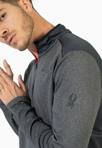 Szary sportowy sweter z wysokim kołnierzem, zdobiony teksturowymi akcentami na ramionach oraz dyskretnym logo na rękawie. Czerwony zamek.