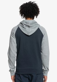 Hooded sweatshirt with navy body and gray raglan sleeves, featuring a soft texture and a kangaroo pocket at the front.