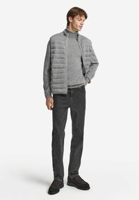 Grau gefütterte Jacke über einem grauen Rollkragenpullover, kombiniert mit dunkelgrauen Jeans und dunklen Schuhen. Die Jacke verfügt über ein gestepptes Design und einen hohen Kragen.