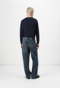 Navy long-sleeve shirt paired with loose, blue denim jeans featuring a back patch and two back pockets. The outfit is completed with black shoes.