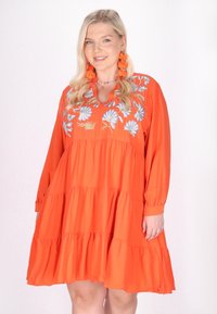 Helles orange Kleid mit langen Ärmeln, das gestufte Rüschen und aufwändige blaue Blumenbestickung am Ausschnitt aufweist.