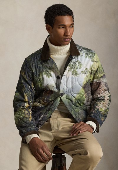 Πανωφόρι με ραμμένη επένδυση που φέρει μια εκτύπωση φύσης με δέντρα σε πράσινο και καφέ, γιακά από βελούδινο ύφασμα και μαύρα κουμπιά. Φοριέται πάνω από μια κρεμ ζιβάγκο μπλούζα.