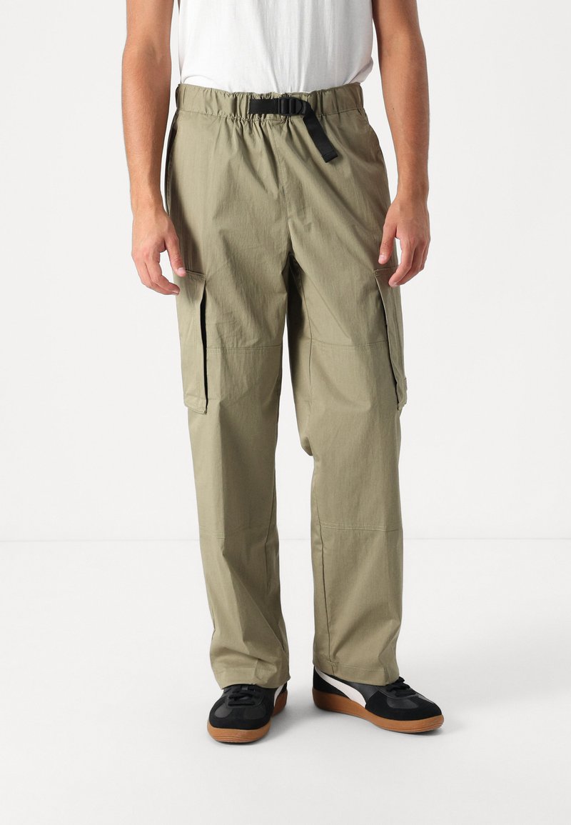 Khaki cargo pants with an elastic waistband and adjustable black strap, featuring side pockets and a lightweight, textured fabric.