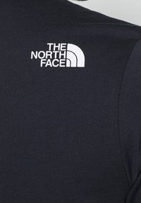 Camiseta de tela negra con textura acanalada, que presenta un logo blanco de "The North Face" en la parte superior izquierda.