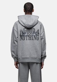 Felpa grigia con cappuccio caratterizzata da una grande grafica nera "GOOD FOR NOTHING" con farfalle sul retro. Realizzata in tessuto morbido, vestibilità relaxed e tasca a marsupio.