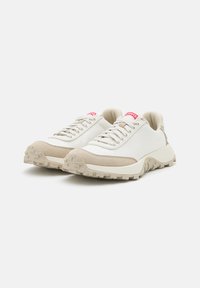 White and beige sneakers with textured suede and mesh upper, thick rubber sole, and red brand logo on the tongue.