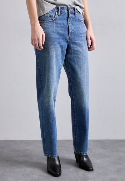 Jean en denim bleu clair à coupe décontractée, taille haute, design à cinq poches et surpiqûres contrastantes, associés à des bottes noires à talons.