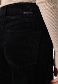 Pantalon en velours côtelé noir avec une surface texturée, doté de poches plaquées et d'une étiquette cousue portant la mention "Marc O'Polo DENIM" sur la taille.