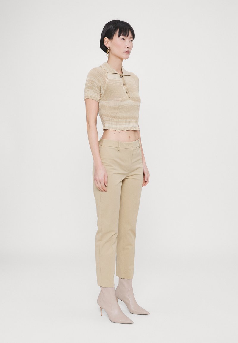 Beige strikket polo skjorte med krage og knapper, kombinert med beige tettsittende bukser og nude ankelstøvler. Glatt tekstur, kort design.