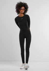 Svart langermet topp med en tettsittende design som har en liten tekstlogo, kombinert med svarte tettsittende leggings og hvite joggesko.