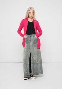 Cardigan rosa, top nero con bottoni, gonna maxi grigia con stampa a serpente e spacco frontale, indossata con sneaker bianche e nere. Texture liscia e design casual.