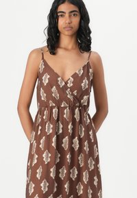 Robe brune à motifs avec des motifs de feuilles, en tissu léger, décolleté en V, bretelles fines réglables, taille élastique et poches latérales.