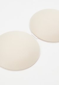 Beige adhesive breast pads with a smooth, textured surface, round shape, and a thin edge, designed for discreet support.