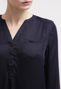 Navy blue, długosleeve bluzka z gładkiego, satynowego materiału. Posiada dekolt w serek, sześć guzików oraz małą kieszonkę na lewej stronie.