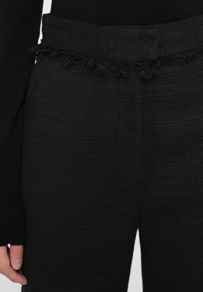 Black textured pants with a fringed waistband. The fabric has a woven appearance, displaying rich depth and subtle variations in texture.