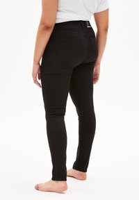 Jeans skinny negros en una tela de mezclilla elástica, con una cintura alta, bolsillos traseros y un ajuste ceñido a lo largo de las piernas hasta los tobillos.