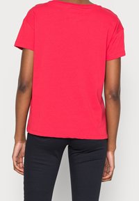 Czerwona bawełniana koszulka z krótkim rękawem, luźny krój i okrągły dekolt. Gładka tekstura, bez widocznych wzorów ani zdobień.