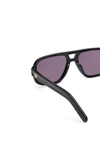 Czarne okulary przeciwsłoneczne o geometrycznym wzorze, z purpurowymi szkłami i złotym akcentem logo po bokach. Gładka plastikowa oprawa i ramiona.