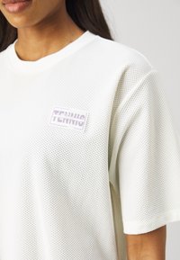 Tricou din plasă albă cu mâneci scurte, decolteu rotund și un logo rectangular violet pe care scrie "TENNIS" cusut pe față.