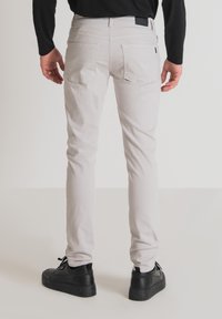 Pantalones ajustados de color gris claro fabricados en algodón, con dos bolsillos traseros y una textura sutil. Combinados con zapatillas negras.