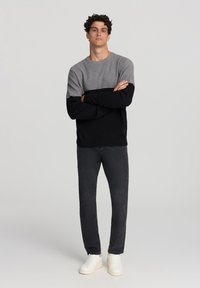 Szary i czarny sweter z długim rękawem w stylu color-block, zestawiony z ciemnymi dżinsami i białymi sportowymi butami. Miękka tekstura, okrągły dekolt i luźny krój.