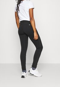 Zwarte leggings met een gladde textuur, hoge tailleband en zijpaneel details, gecombineerd met een wit t-shirt en witte sportieve schoenen.