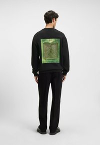 Felpa nera con un motivo centrale a labirinto verde sul retro, con la scritta "HUGO" posizionata sopra il labirinto. Stile casual, polsini a costine.